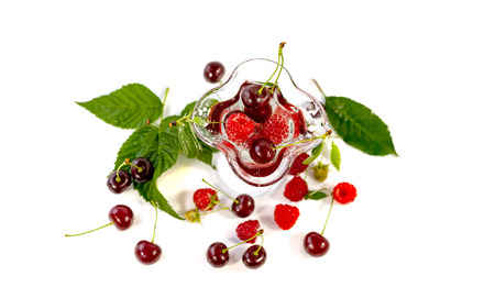 Cherries and raspberries in a glass bowl and beyond on a white background