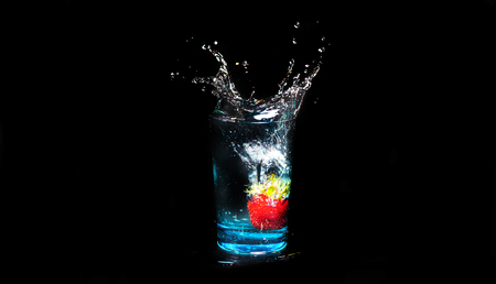 Strawberries fall in a glass of water on a black backgroundの写真素材