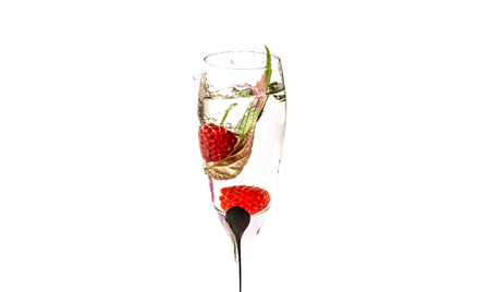 The process of falling raspberries in a glass of champagne with water on a white backgroundの写真素材