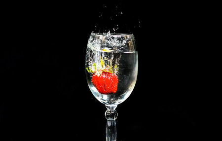 Strawberries fall in a glass of water on a black backgroundの写真素材
