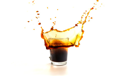 A cup of coffee with splashes in the process of spilling on a white backgroundの写真素材