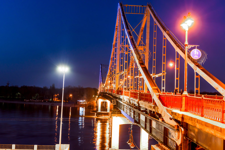 Pedestrian metal bridge with colored lights through the river at nightの写真素材