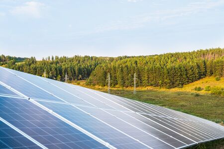 Rows of solar panels on a background of supports and power lines among the forestの写真素材
