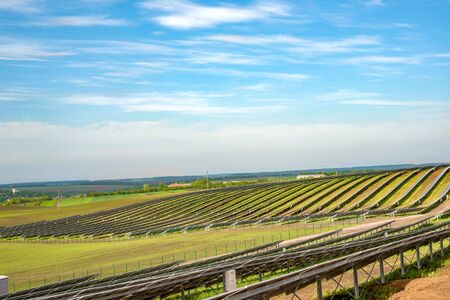 Rows of solar panels on steep hills fields on sky background - rear view