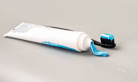 White tube with toothpaste and black toothbrush on a gray background