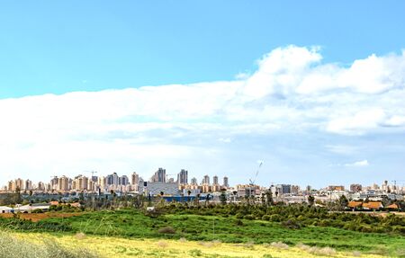 Modern city on the horizon on a background of blue sky with white clouds and green field
