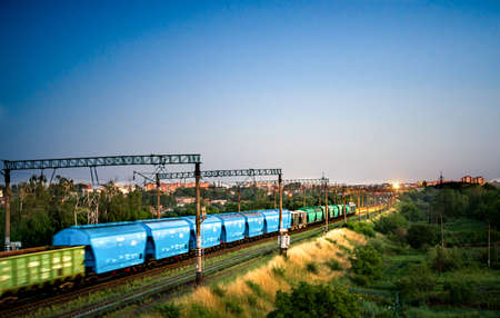 Train with freight cars while moving in the evening against the background of entering the city