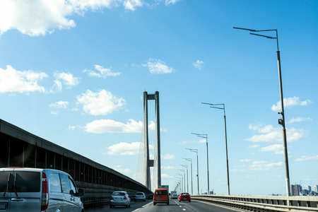 Exit on the highway to the concrete bridge across the river on a background of blue sky and city