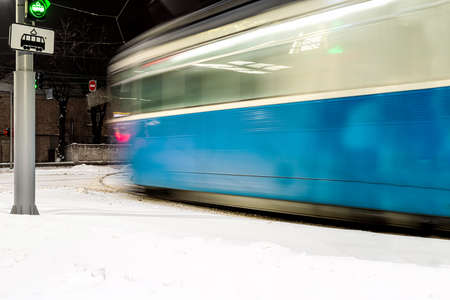 Blurred silhouette of a blue tram in motion at a turn on a city street at night in winterの写真素材