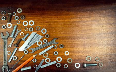 Various tools and metal washers, nuts, staples for stapler on a background of brown wood textureの写真素材