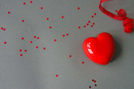 Red heart-shaped cake with a ribbon and red sparkle stars on a gray backgroundの写真素材