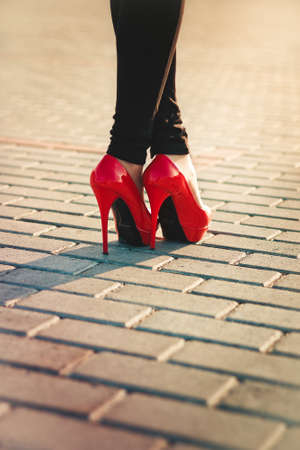 Beautiful female legs in glossy red shoes with pavement in the backgroundの写真素材