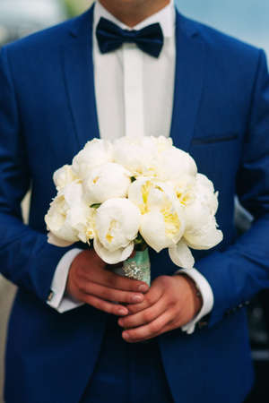 Gentle wedding bouquet of white  peonies in the hands of the groomの写真素材