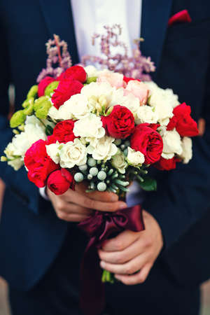 Stylish, beautifully decorated wedding bouquet of white and red roses in the hands of the groomの写真素材