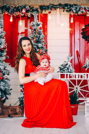 Cheerful mom in red dress and her little daughter in decorated christmas room.の写真素材