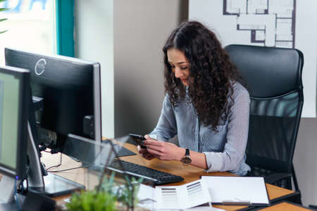 Young female architect using smart phone at workplace in the modern office.の写真素材