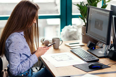 Young female architect using smart phone at workplace in the modern office.の写真素材