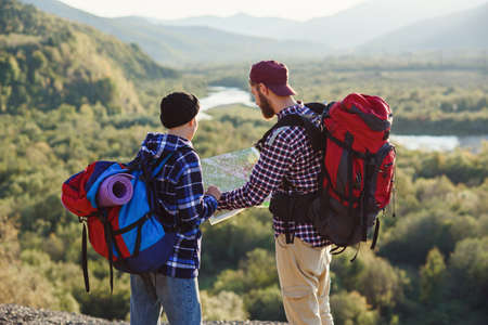 Young couple traveling together in mountains. Happy hipster man and his girlfriend with backpacks planning route by looking at paper map. Traveling, tourism and friendship concept.の写真素材