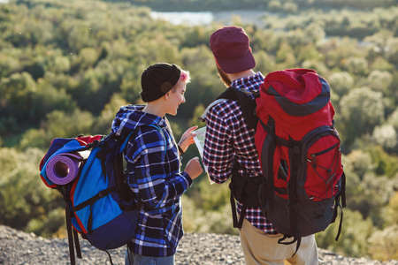 Young couple traveling together in mountains. Happy hipster man and his girlfriend with backpacks planning route by looking at paper map. Traveling, tourism and friendship concept.の写真素材