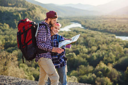 Young couple traveling together in mountains. Happy hipster man and his girlfriend with backpacks planning route by looking at paper map. Traveling, tourism and friendship concept.の写真素材