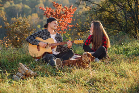 Young man playing on the guitar for his lovely girlfriend. Happy couple with guitar resting on picnic in spring park.の写真素材