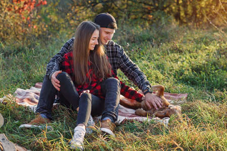 Happy caucasian couple with guitar resting on picnic in spring park. Young man and his girlfriend playing with their funny dog.の写真素材