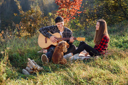 Young man playing on the guitar for his lovely girlfriend. Happy couple with guitar resting on picnic in spring park.の写真素材