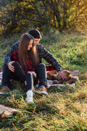 Happy caucasian couple with guitar resting on picnic in spring park. Young man and his girlfriend playing with their funny dog.の写真素材