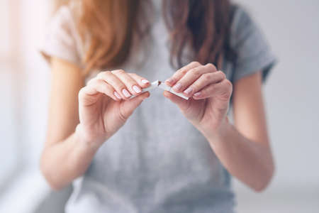 Portrait of beautiful smiling girl holding broken cigarette in hands. Happy female quitting smoking cigarettes. Quit bad habit, health care concept. No smoking.の写真素材