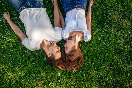 Romantic couple of young people lying on grass in park. They lay on the shoulders of each other and hold hands together. They look happy. View from above.の写真素材