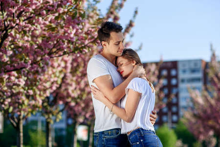 Couple hugs near sakura trees in blooming garden. Couple in love spend time in spring garden,...