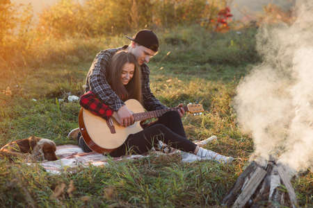 Young man playing on the guitar for his lovely girlfriend. Happy couple with guitar resting on picnic in spring park.の写真素材