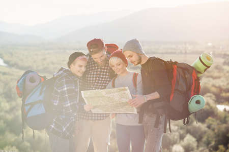 Group of people hiking and looking at map during their adventure. Two men and two women, hikers exploring mountains. Happy friends with backpacks using map to choose right direction.の写真素材