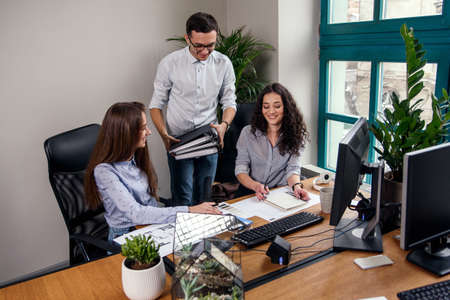 Young firm manager brings folders with work tasks for his employees. Creative people or advertising business concept. Young beautiful people working in office together.の写真素材