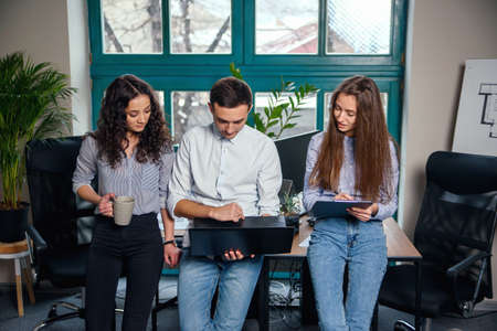 Business team of young architects or designers creating new project while working in the modern stylish office with big window on background.の写真素材