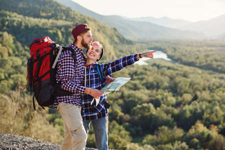Young couple traveling together in mountains. Happy hipster man and his girlfriend with backpacks planning route by looking at paper map. Traveling, tourism and friendship concept.の写真素材