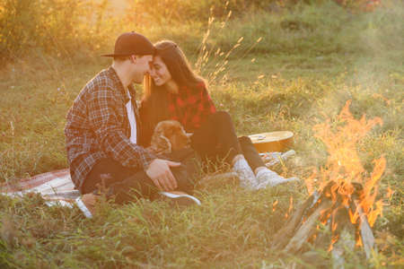 Happy caucasian couple in casual clothes with their funny dog sitting on the lawn in spring park. Young beautiful girl nd her handsome boyfriend leaned against each other at the nature.の写真素材