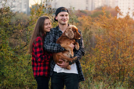 Happy caucasian couple dressed casual clothes walking with their dog on the lawn at park. Beautiful girl leaned against her boyfriend and theyre enjoying at the nature.の写真素材