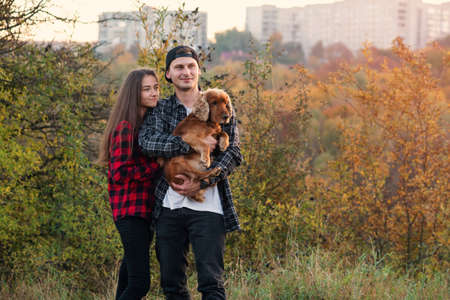 Happy caucasian couple dressed casual clothes walking with their dog on the lawn at park. Beautiful girl leaned against her boyfriend and theyre enjoying at the nature.の写真素材