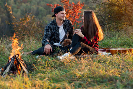 Happy caucasian couple with their funny dog sitting on the lawn in spring park. Young man and his girlfriend enjoying at the nature at sunset.の写真素材