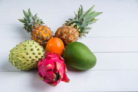 Exotic fresh summer fruits on white background. Dragon fruit, pineapple, persimmon, mango, annona cherimola flat lay with free copy space.の写真素材