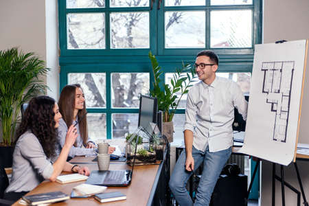 Young caucasian male architect showing building plans on new house to his female coworkers in the...