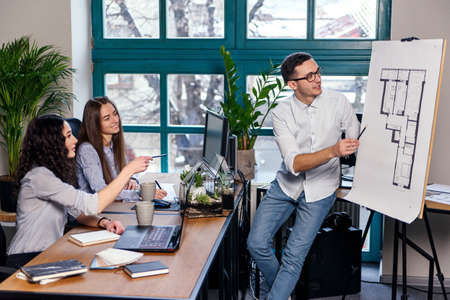 Chief engineer talking about new creative idea in the building plans while two female coworker noting in the notebook in the modern office.の写真素材