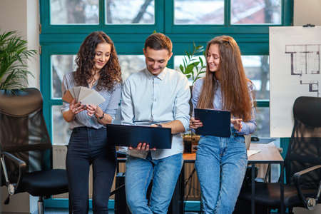 Business team of young architects or designers creating new project while working in the modern stylish office with big window on background.の写真素材