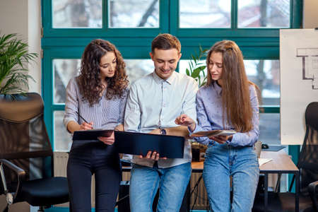 Business team of young architects or designers creating new project while working in the modern stylish office with big window on background.の写真素材