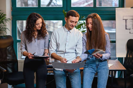 Team of young caucasian engineer standing near table while talking about new idea about building plans in the stylish modern office.の写真素材