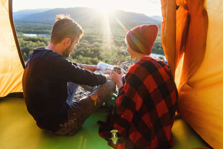 Young man and his girlfriend exploring map in the mountain during sunny day while they are sitting in the tent. View from back.の写真素材