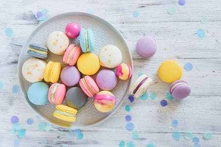 Multicolored french macaron cakes on blue plate and white wooden background. White, yellow, pink, purple and grey french macarons with fresh berries.の写真素材