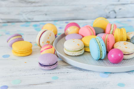 Multicolored french macaron cakes on blue plate and white wooden background. White, yellow, pink, purple and grey french macarons with fresh berries.の写真素材