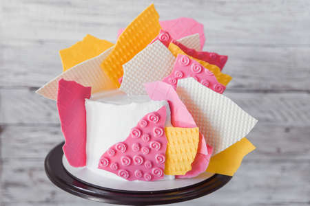 Decorative elements of stylish colored cake staying on black tray on the white wooden background. Birthday party celebration gift.の写真素材